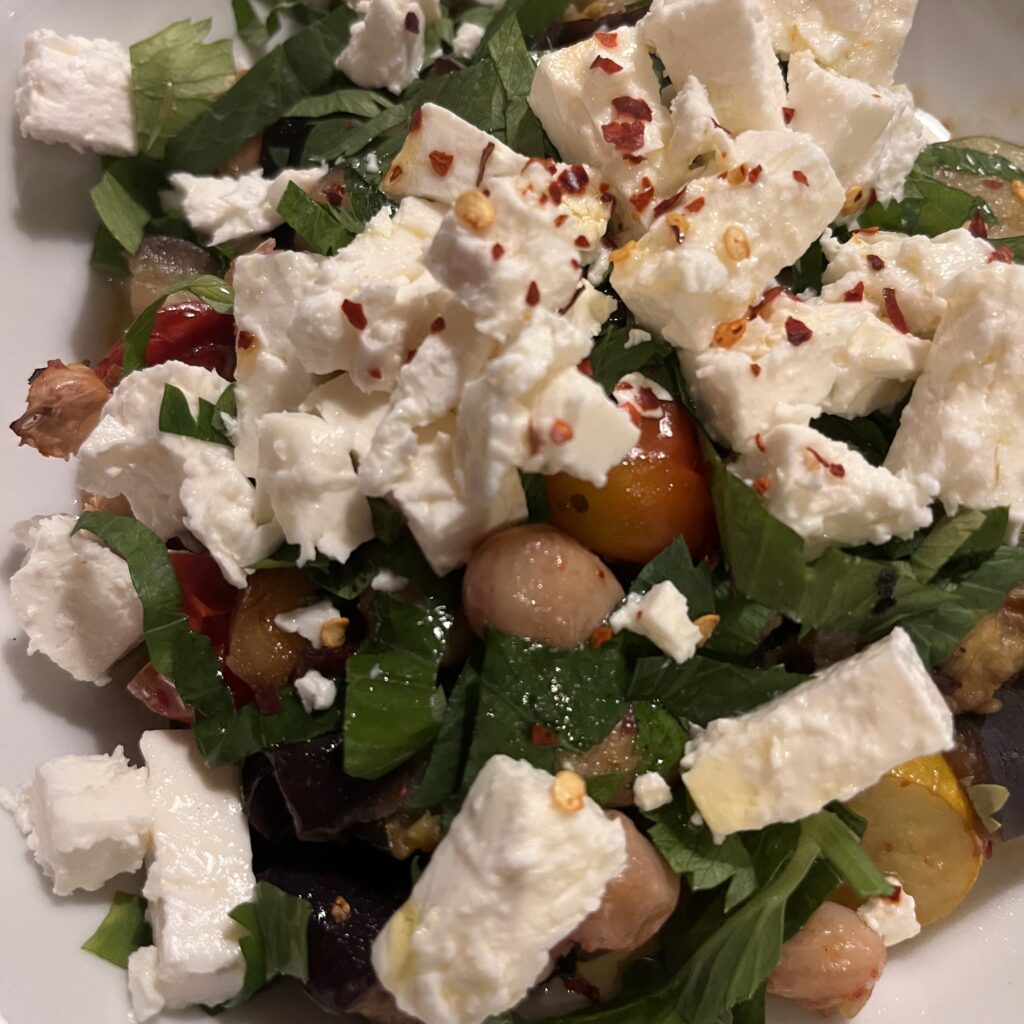 Feta cheese, sprinkled with chilli flakes on top of roasted courgettes, beans, celery leaves and cherry tomatoes
